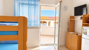 Una habitación con cama, una kitchenette pequeña, televisión y vista a un edificio.