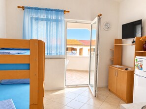 Ein Zimmer mit Bett, einer kleinen Küchenzeile, einem Fernseher und Blick auf ein Gebäude.