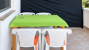 Un balcón con mesa y sillas, una pantalla de privacidad negra y un equipo de aire acondicionado.