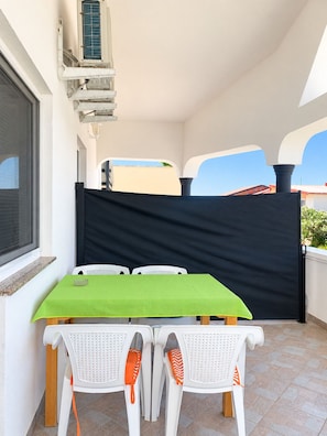 Ein Balkon mit Tisch und Stühlen, einer schwarzen Sichtschutzwand und einer Klimaanlage.