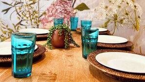 A dining table set with blue glassware and plates, surrounded by various flowers and plants. - Twickenham House Sleeps 7 with Parking - Isleworth (Greater London)