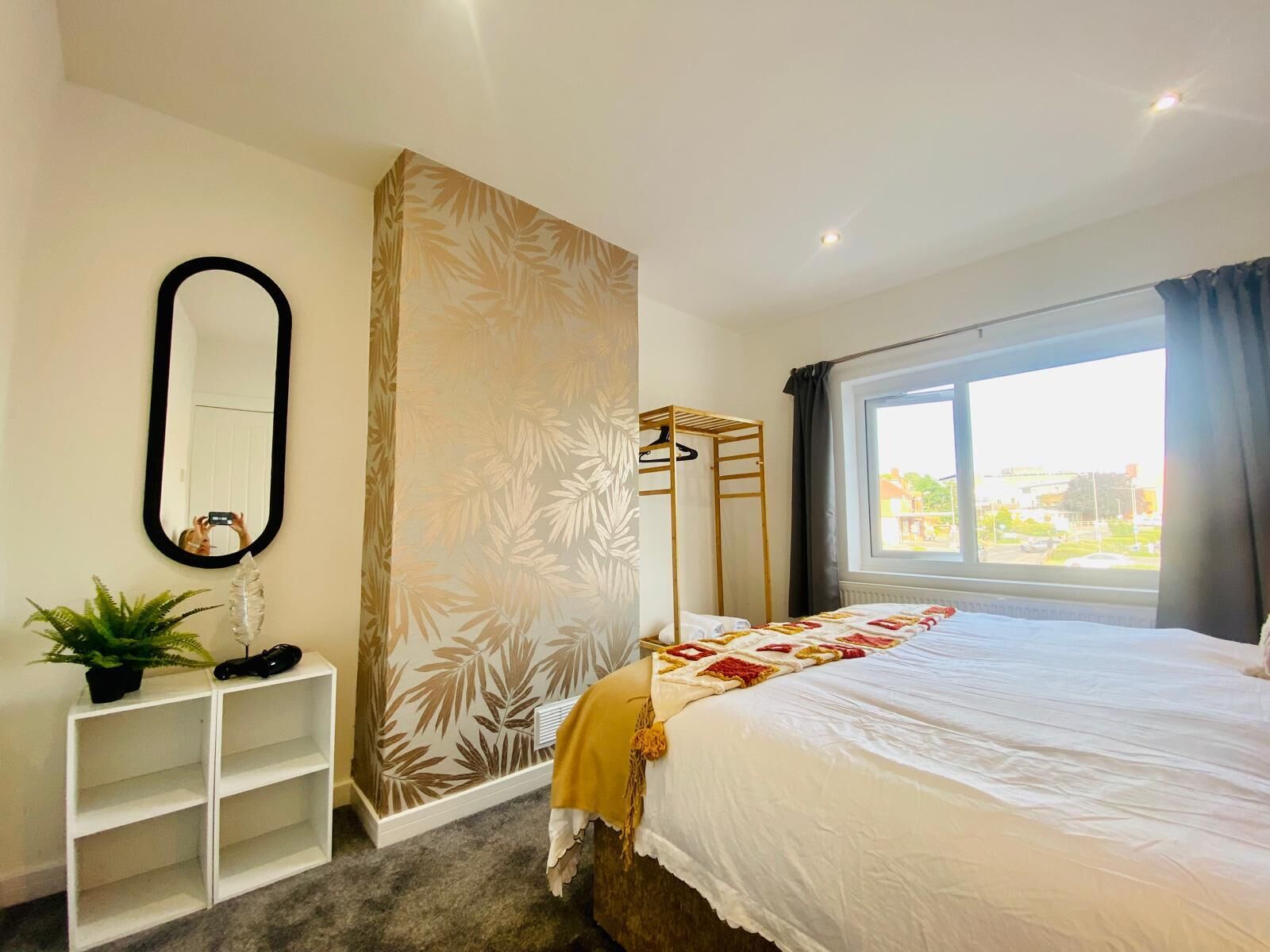 A bedroom with a bed, a wardrobe, a mirror, a plant, and a window with a view.