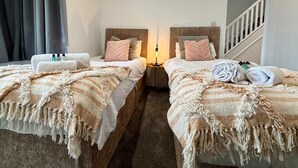 A hotel room with two beds, each with a headboard, a nightstand, and a lamp. - Twickenham House Sleeps 7 with Parking - Isleworth (Greater London)