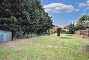 A residential backyard with a lawn, a tall tree, and a wooden fence.