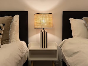 A bedroom with two beds, a nightstand with a lamp, and a plain wall.