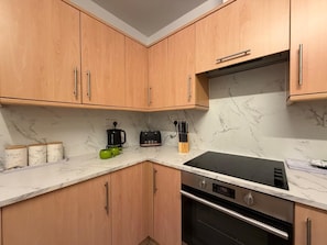A modern kitchen with wooden cabinets, a black stove, and a marble countertop.