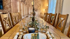 Una larga mesa de madera dispuesta para una comida, con copas de vino, una vela y servilletas enrolladas.