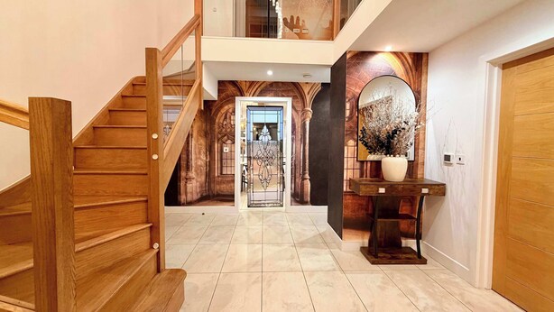 Un amplio pasillo con una escalera de madera que lleva a un segundo piso, un espejo decorativo y un suelo de baldosas.