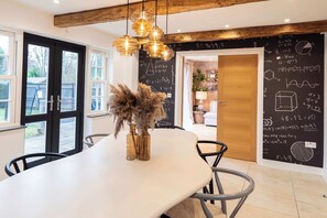 Un espace repas avec une longue table, des chaises et des lampes suspendues. Un tableau noir, sur lequel sont écrites des équations mathématiques, est accroché au mur.