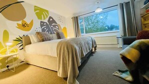 Une chambre à coucher avec un lit, une table de chevet, une chaise, une fenêtre et une vue sur les arbres à l’extérieur.