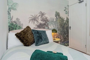 A bedroom with a bed, pillows, a green blanket, and a mural of a tropical scene on the wall. - Norwich Spacious 5 Bed House (Norfolk)