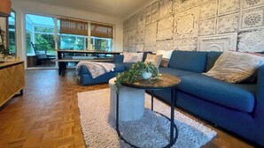 Un salon moderne avec un canapé bleu, une table basse ronde agrémentée d'une plante et un mur orné d'un motif.