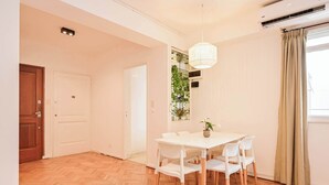 A room with a wooden herringbone floor, a white dining table with chairs, a pendant light, a potted plant, and a window with curtains. - MOT  Rentals + Laprida 1300 - 3 Bd 2 Ba in Recoleta! (Buenos Aires)