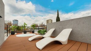 Una terrazza sul tetto con due poltrone bianche, una vasca idromassaggio e piante in vaso.