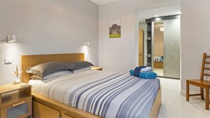 Un dormitorio moderno con cama, mesitas de noche, una silla y una puerta que da a otra habitación.