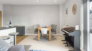 Una sala de estar moderna con comedor, un piano y una encimera de cocina con copas de vino.