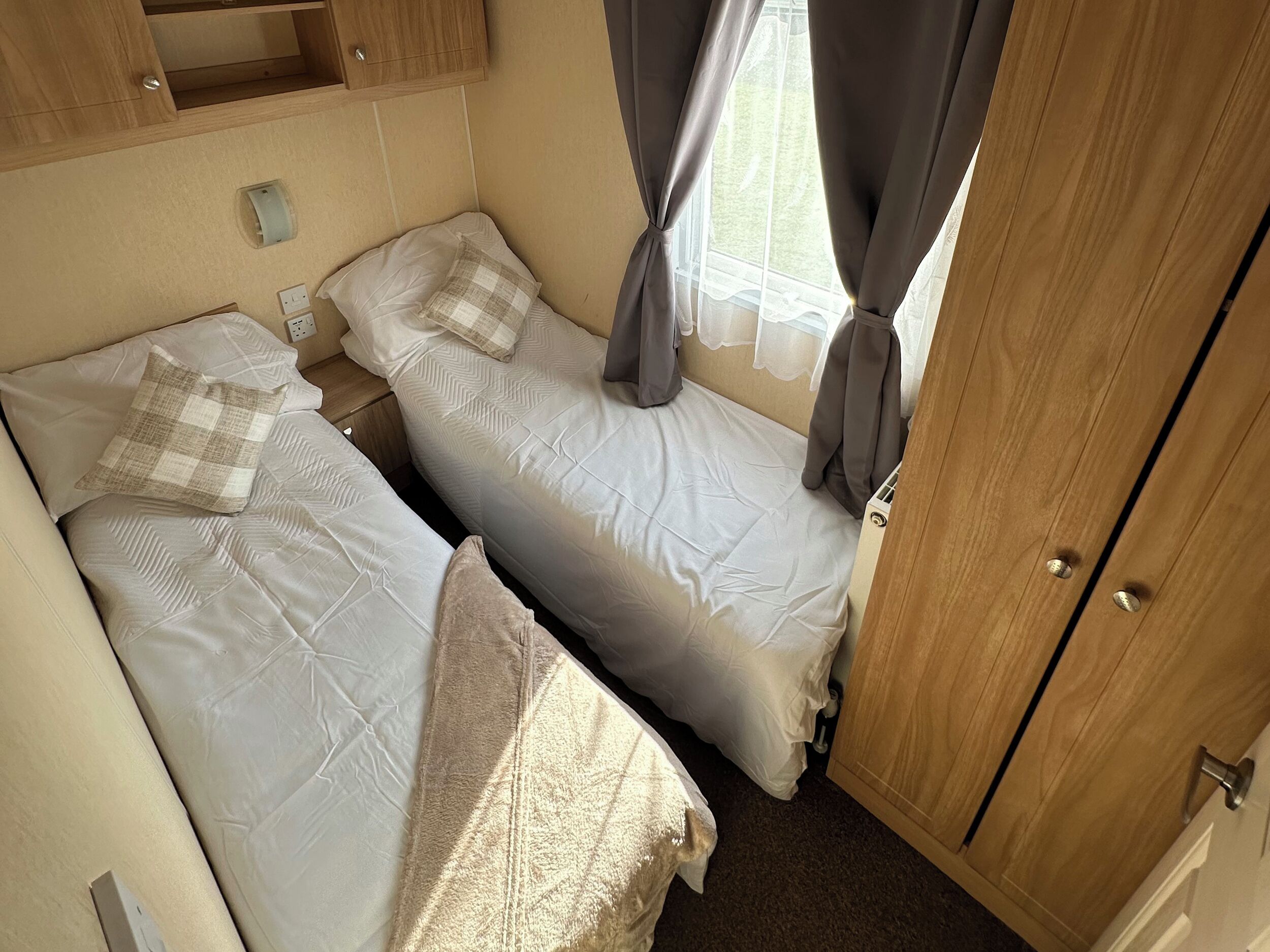 Un dormitorio pequeño con dos camas, un armario de madera y una ventana con cortinas.
