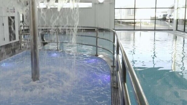 A large indoor pool with a central water feature and a glass barrier. - C43 The Hideout (Abergele)