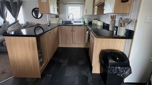 A compact kitchen with wooden cabinets, a black countertop, a sink, and a fire extinguisher. - C43 The Hideout (Abergele)