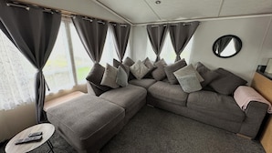 A modern living area with a sectional sofa, a small round coffee table, and a mirror on the wall. - C43 The Hideout (Abergele)