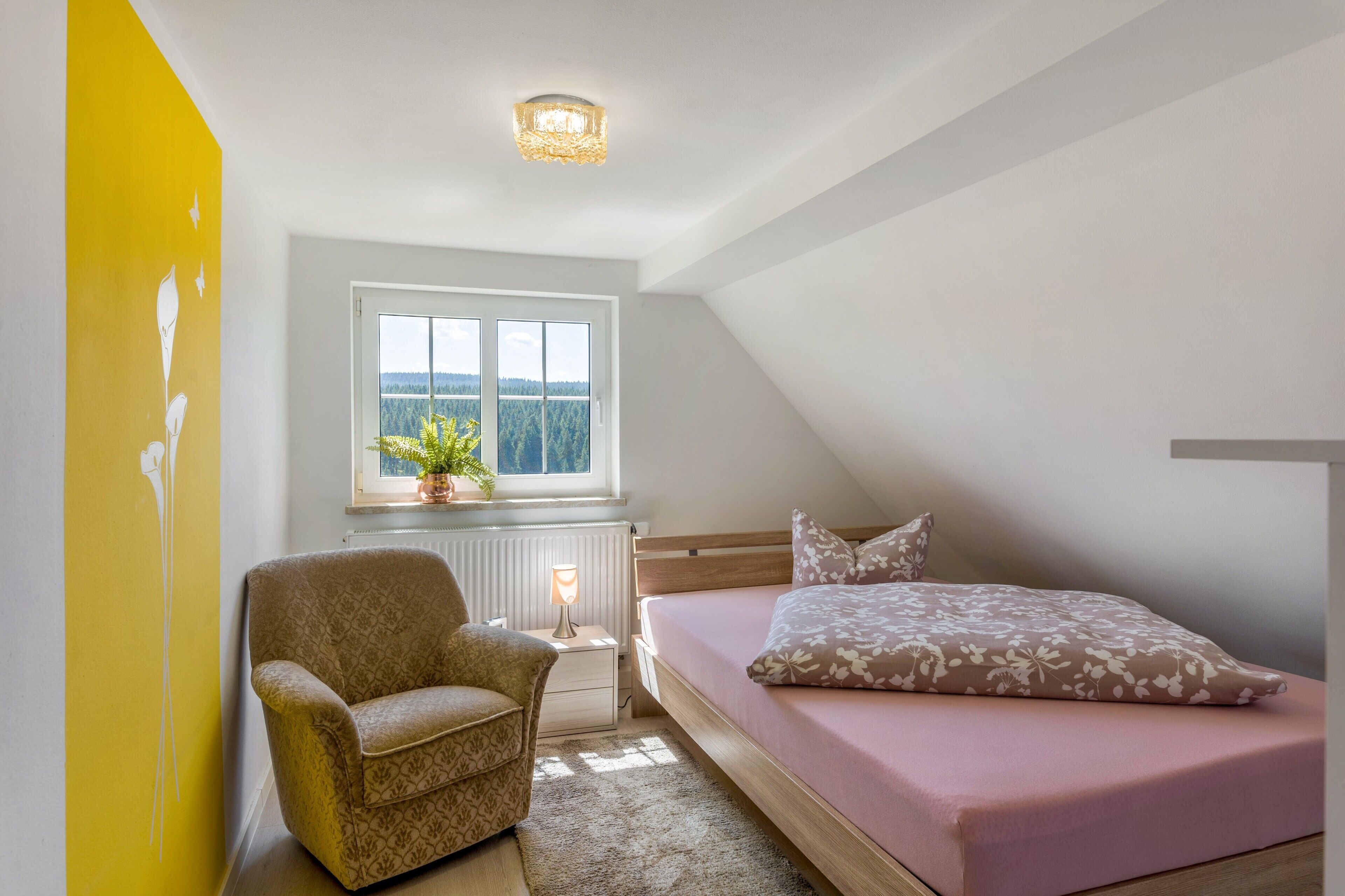 A bedroom with a bed, a chair, a window with a view, and a radiator.