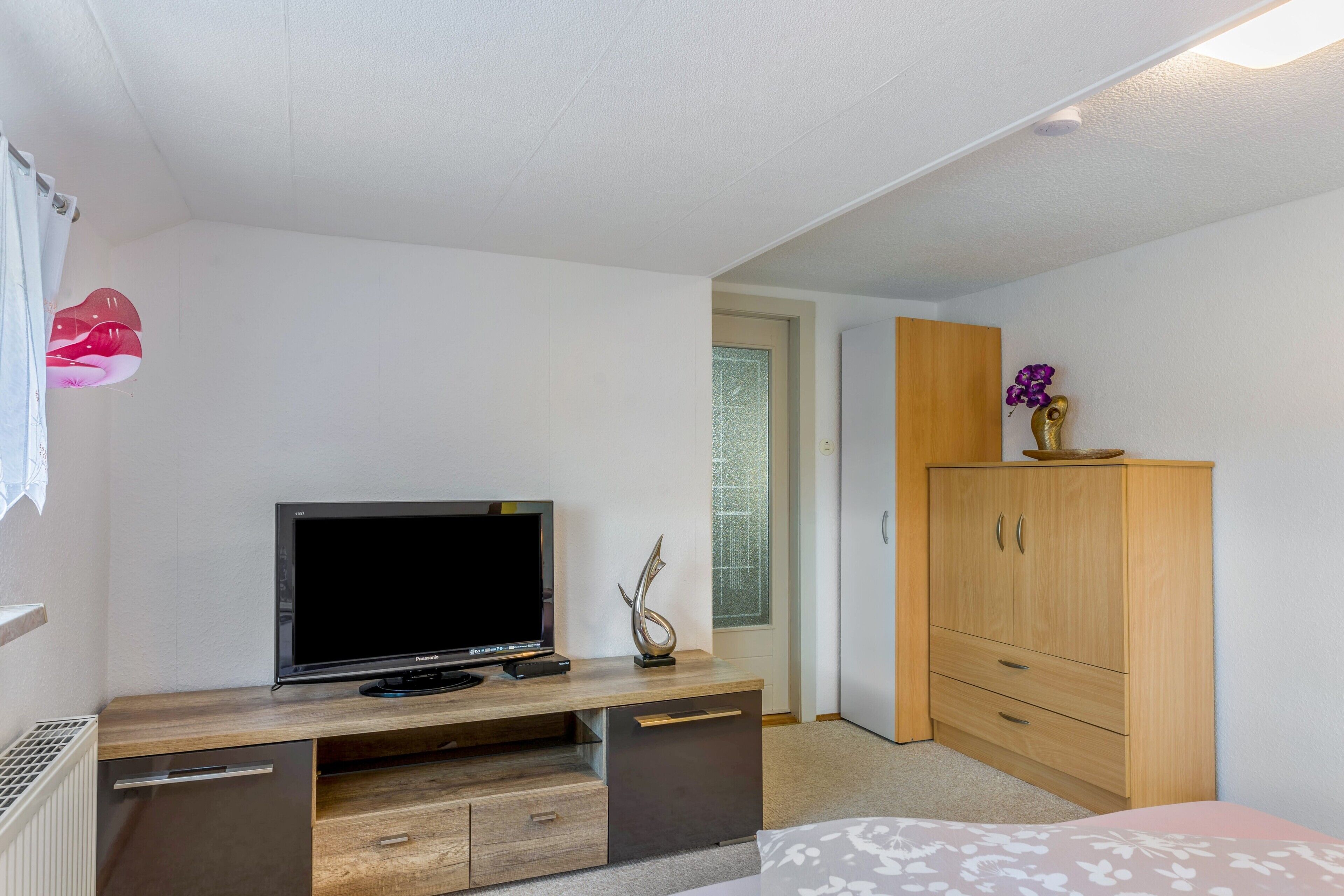 A bedroom with a TV, wooden wardrobe, and a bed.
