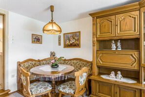 Un coin repas avec une table ronde, des chaises à motifs floraux, un buffet en bois orné de figurines décoratives et des œuvres d’art accrochées au mur.
