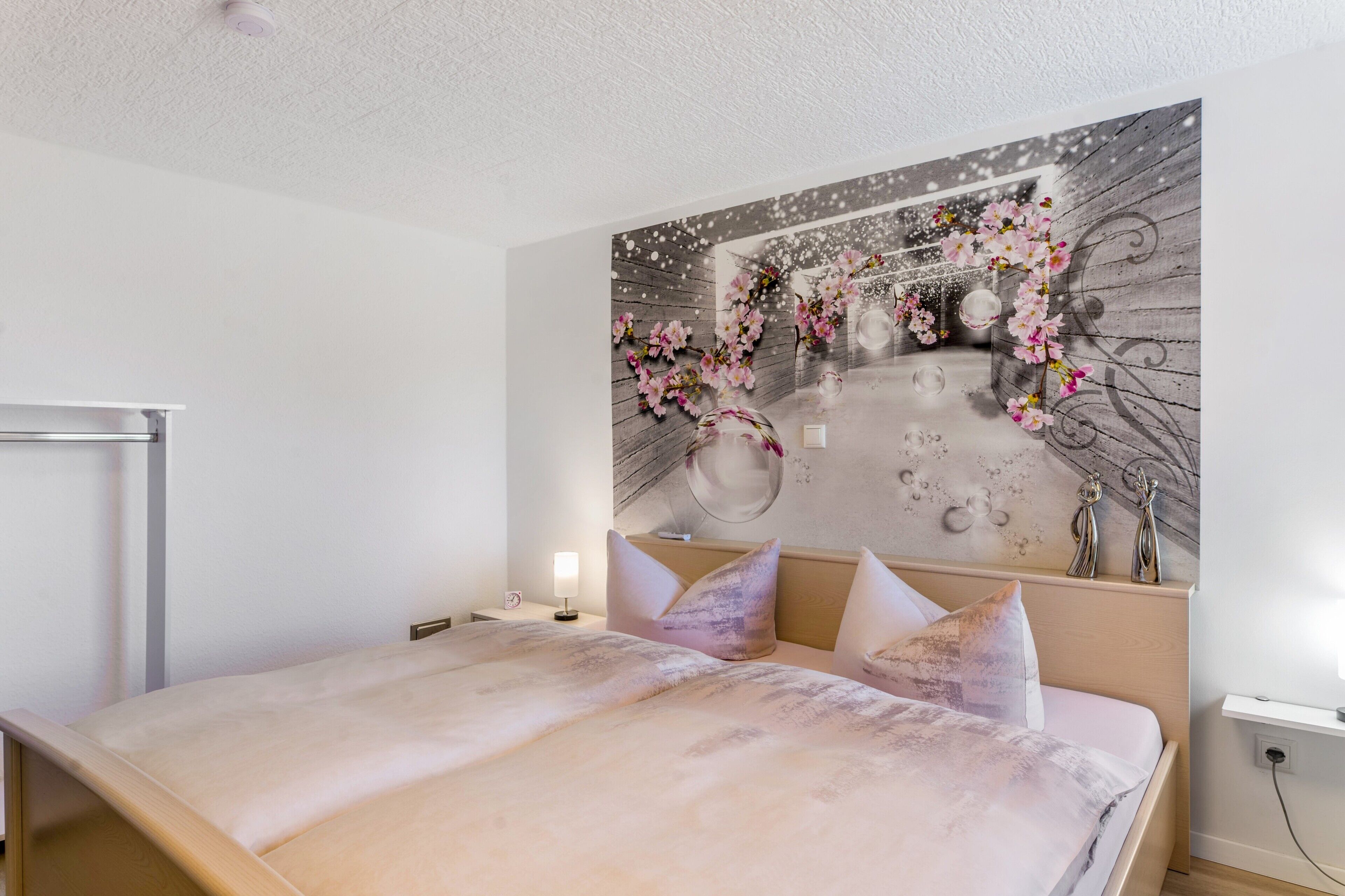 Ein Schlafzimmer mit einem Bett, einem Nachttisch, einer Wandlampe und einem dekorativen Wandbild.