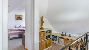 A bedroom with a bed, a painting, and a shelf with toys and puzzles.