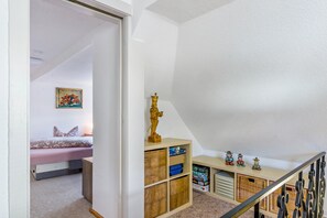 A bedroom with a bed, a painting, and a shelf with toys and puzzles.