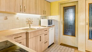 A compact kitchen with wooden cabinets, a microwave, a sink, and a door with a frosted glass panel.