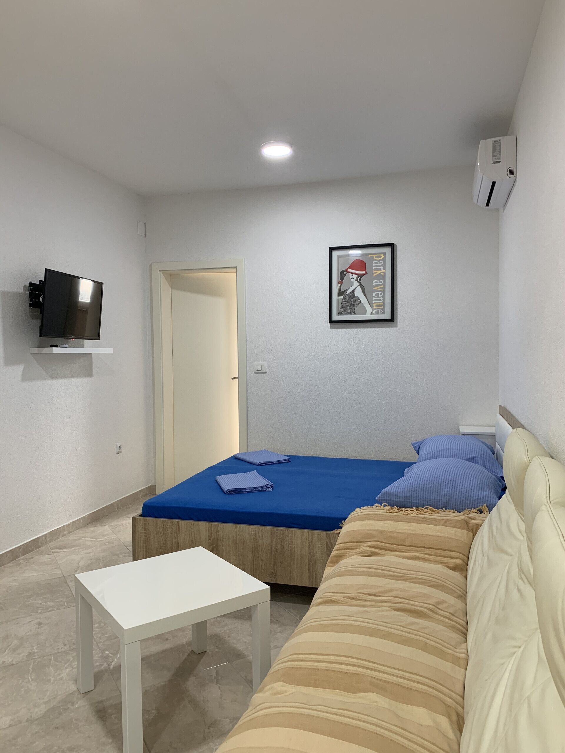Una habitación pequeña y moderna con una cama, un sofá, un televisor y un cuadro en la pared.