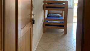 Una habitación con literas, una puerta de madera, una ventana con cortinas y un equipo de aire acondicionado.