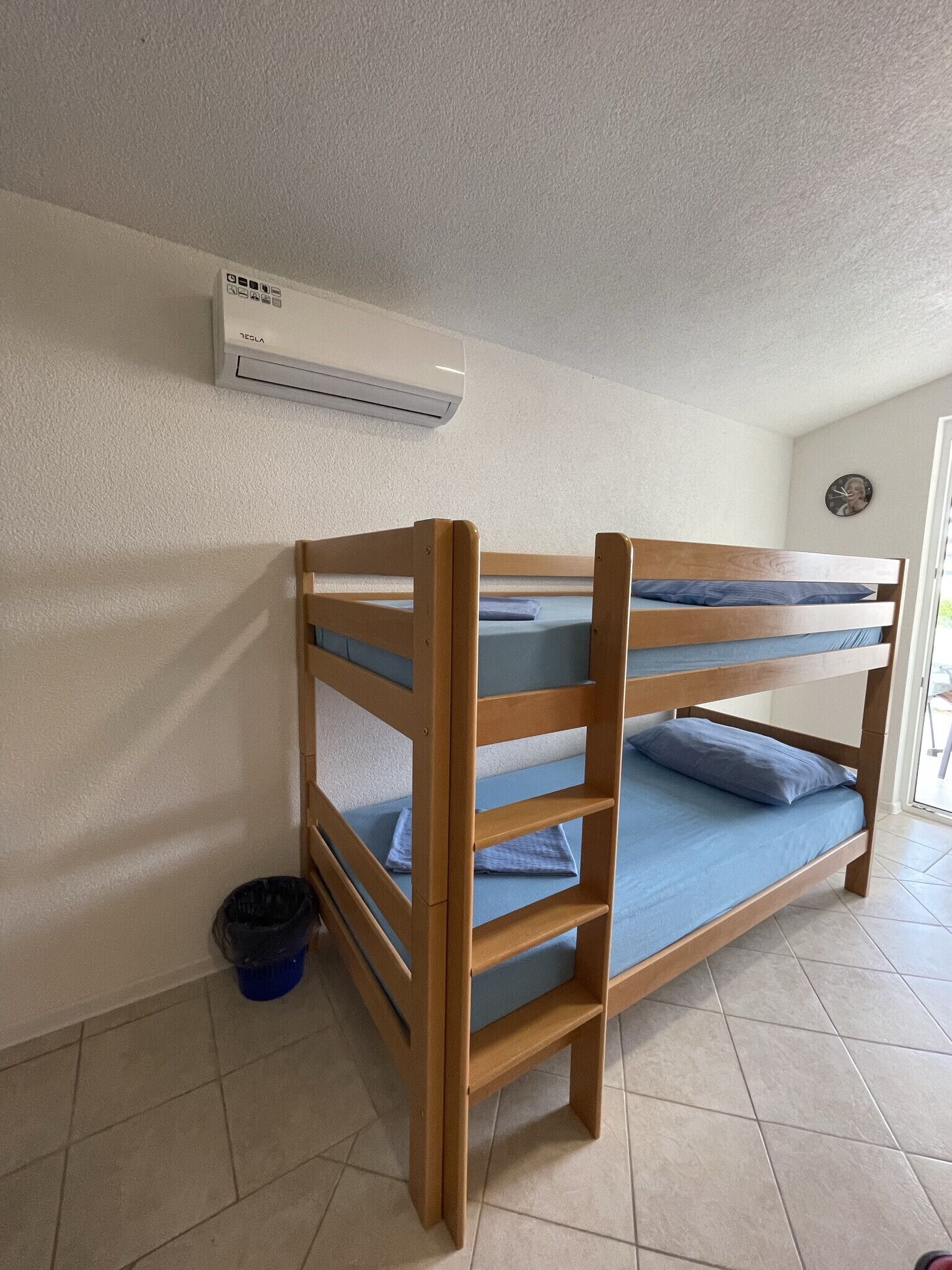 A bunk bed with a ladder, a blue bucket, and an air conditioning unit on the wall.