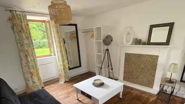 A room with a black sofa, a white coffee table, a tripod, a fireplace, and a large mirror. - French Countryside Retreat With Jacuzzi (Plouasne)