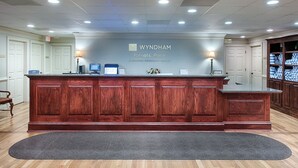 Un mostrador de recepción en Wyndham Patriots' Place con detalles de madera, una computadora y un cartel en la parte superior.