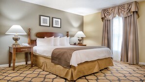 Una habitación de hotel con una cama grande, dos mesitas de noche con lámparas, un cabecero, una alfombra estampada y una ventana con cortinas.