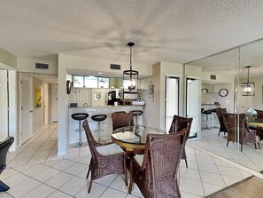 A spacious kitchen with a central island, bar stools, and a dining table with wicker chairs. - Edgewater Villa #2001 | Close to Beach with Amazing Resort Amenities (Panama City Beach)