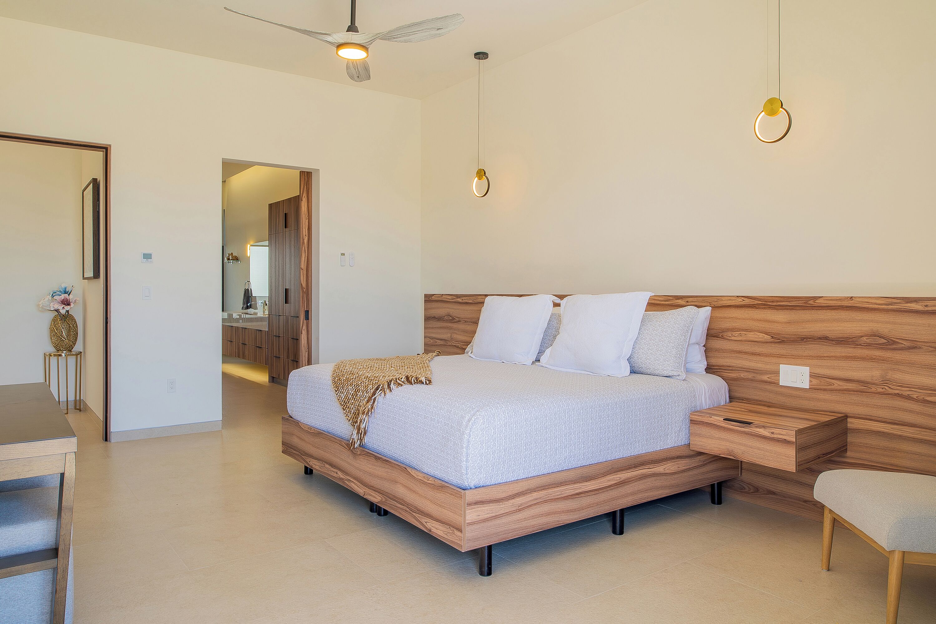 Une chambre moderne avec une tête de lit en bois, un lit recouvert de linge de maison blanc, une table de chevet et un luminaire suspendu.