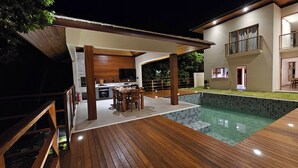 A modern house with a wooden deck, a swimming pool, and a kitchen area. - Luxury house in contact with nature and private pool in Praia do Forte (Açu da Torre)