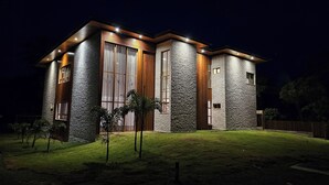 A modern house with a stone facade, large windows, and a well-lit entrance. - Luxury house in contact with nature and private pool in Praia do Forte (Açu da Torre)
