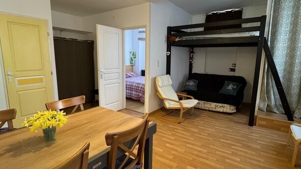 Una habitación acogedora con literas, una mesa de comedor con sillas y un pequeño rincón de descanso con cojín.
