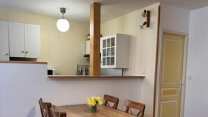 Un comedor con una mesa y sillas de madera, un jarrón de flores amarillas, y una lámpara colgante arriba.