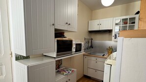 Una cocina compacta con muebles blancos, microondas, tostadora y refrigerador.