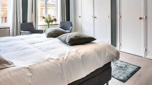 A modern bedroom with a large bed, two chairs, a desk, and a wardrobe. - The Rose Suites (Bruges)