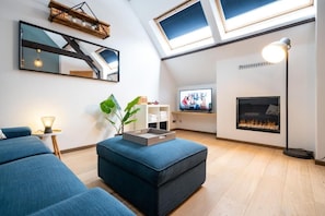 A modern living room with a loft-style ceiling, a fireplace, a television, and a large window. - The Rose Suites (Bruges)