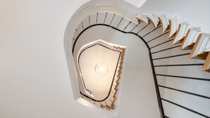 A spiral staircase with a white wall and a circular skylight at the top. - The Rose Suites (Bruges)