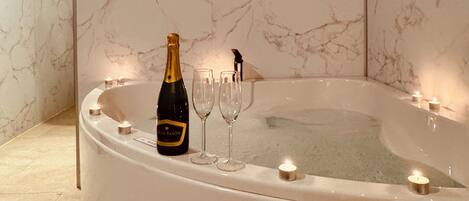 Une baignoire en marbre, une bouteille de champagne et deux verres.
