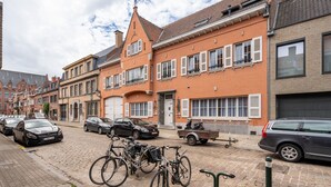 A cobblestone street lined with historic buildings, parked cars, and bicycles. - The Rose Suites (Bruges)
