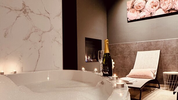 A modern bathroom with a large bathtub, a champagne bottle, candles, and a floral artwork on the wall. - The Rose Suites (Bruges)